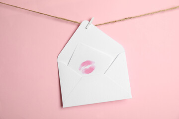 White envelope and card with lip print hanging on twine against pink background. Love letter