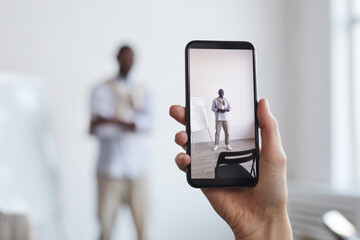 Close up of unrecognizable woman taking photo of African-American businessman standing by whiteboard, focus on smartphone screen, copy space