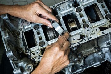 The hand of an auto mechanic picks up the engine connecting rod bearing in check with the engine's crankshaft on background.	