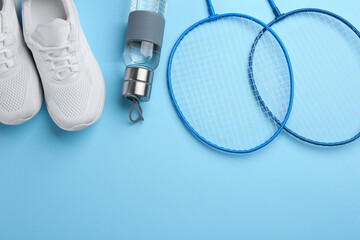 Badminton rackets, bottle and shoes on light blue background, flat lay. Space for text