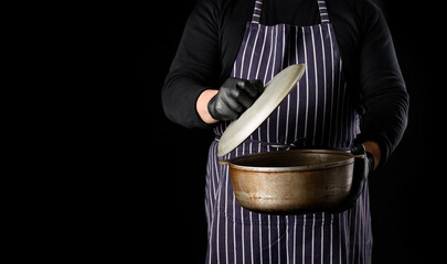  man chef in a striped apron holds an aluminum cauldron with a lid