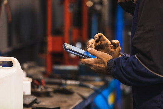 Mechanic using cell phone in the workshop. Hands full of grease. Technology concept.