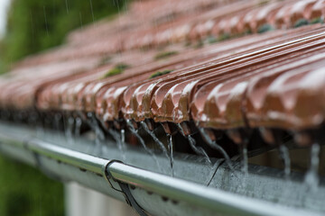 Drops of water flow into the eaves on the house in the rain.
