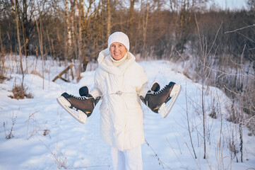 Fototapeta na wymiar Happy elderly senior mature woman in white warm outwear playing with ice skates in sunny snowy winter outdoors. Retired healthy people holiday vacation winter activities, active lifestyle concept.