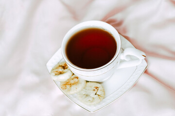 White cup with tea with a saucer, next to dried dates dessert on a silk tablecloth.