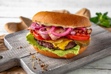 Delicious, juicy hamburger, cheeseburger with beef, cheese, baked vegetables and fruits, onion jam, sauces on wooden background, rustic style.