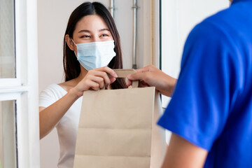 Fototapeta na wymiar Young asian woman, customer wearing face mask protect to pandemic of covid and received bag,cardboard box from delivery man while lockdown,quarantine at entrance, door of home,house.Take away concept.