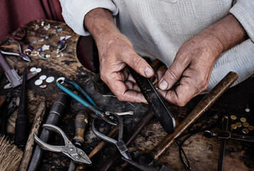 Closeup of an old caucasian man handcrafting a ring with its tools.