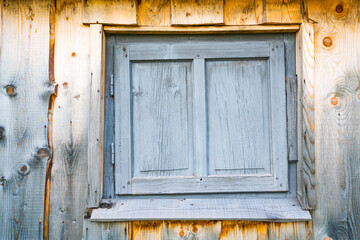 Small closed window in the wooden wall of an old house