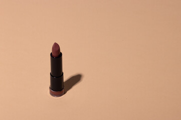 Lipstick on a beige background with shadow. Female cosmetic product for makeup. Copy space.
