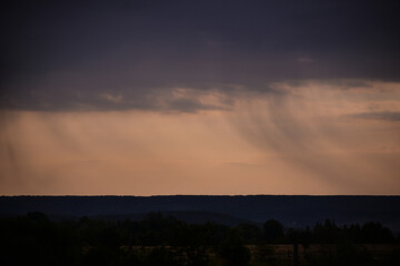 Naklejka na ściany i meble rain seen from afar at sunset. colored clouds on the horizon