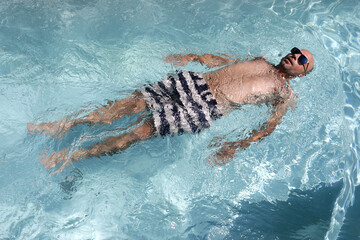 Young bald handsome man floating in a swimming pool wearing sunglasses