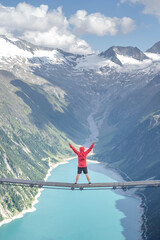 Tourist with red hoody sit on swing bridge looking at glacier reservoir in Austria zillertal Alps