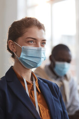 Vertical portrait of young businessman wearing mask and looking away while sitting in audience at business conference