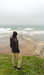 Unrecognisable man looking out to sea. On a cloudy day. Wearing jacket and cap