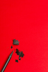 Vertical image.Top view of black pensil, shavings on the bright red surface.Empty space