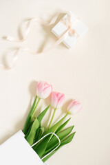 Flat lay composition with pink tulips in paper bag and a gift with a bow on beige background. Greeting card for Valentine's Day, Mother's Day, Birthday. The concept of spring