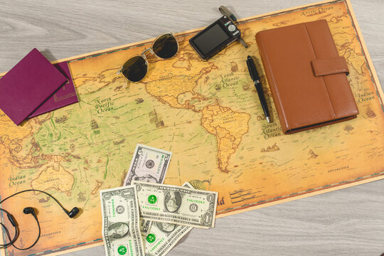 top view of travel concept with passports, travel photo camera, sunglasses, diary and pen to take notes, headphones for listening to music and money bills on a vintage world map