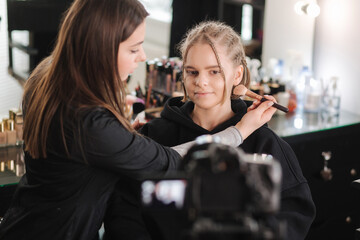 Woman making a video for her blog of making makeup, digital camera on tripod. Young female blogger on camera screen while doing makeup