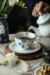 Elegant tea time.Woman pouring tea in classic white and blue cup with floral pattern .