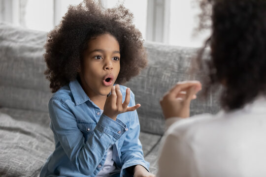 Close up disabled African American girl practicing sign language with mother or teacher, showing symbols, using gestures, interacting, repeating sounds, involved in speaking lesson at home