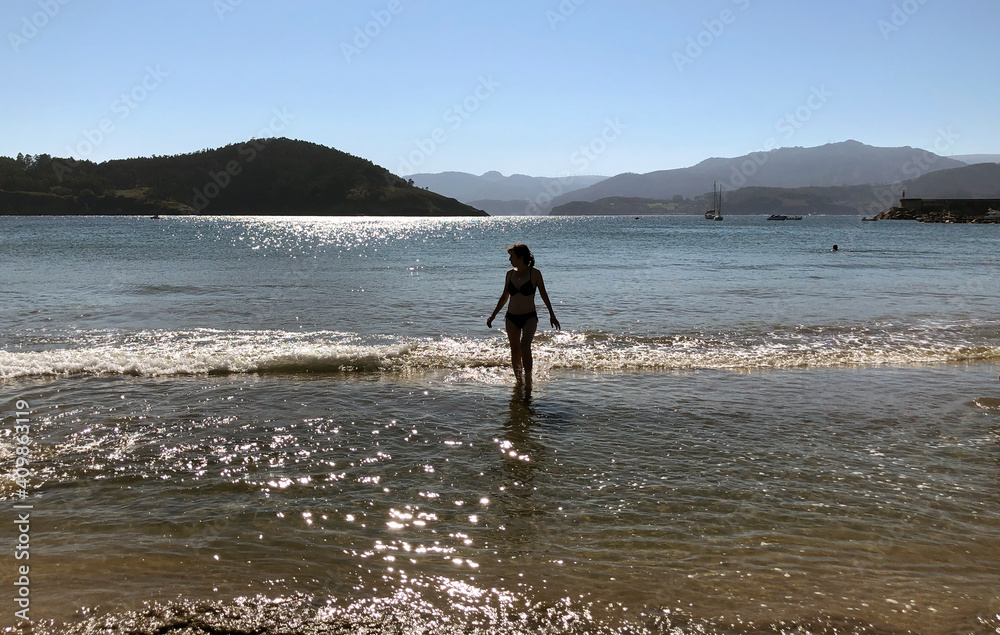 Wall mural Silhouette of woman at the beach, emerging from calm ocean waters with back light. - Wall murals