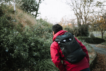 Young man outside with backpack looking at plants