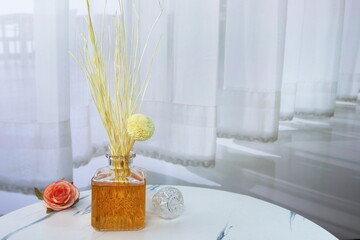 luxury aromatic scented reed diffuser glass bottle display on the grey table for romantic and relax ambient in the white bedroom near the curtain on valentine day