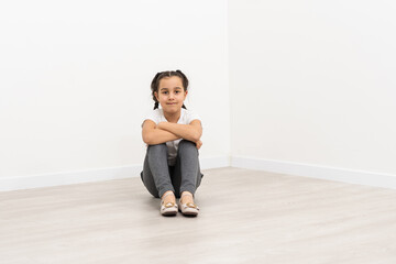 Smiling little girl in full length sitting over white background and looking up