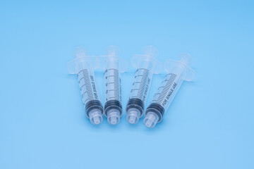 Four clear plastic 5ml syringes isolated against a blue background