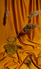 Bertical image.Green glass vase, dried flowers and reeds n the soft silk surface.Decorative elements