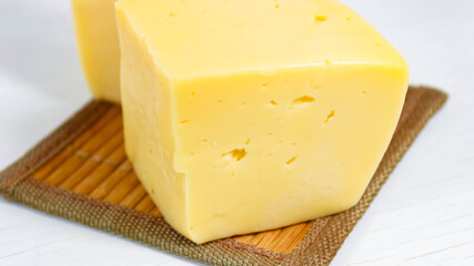 A cut piece of hard cheese close-up on a light background.