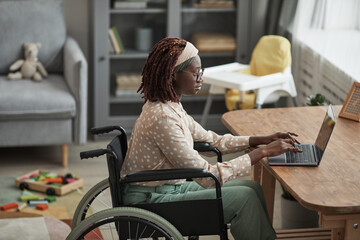 High angle portrait of young African-American woman using wheelchair while working from home with...