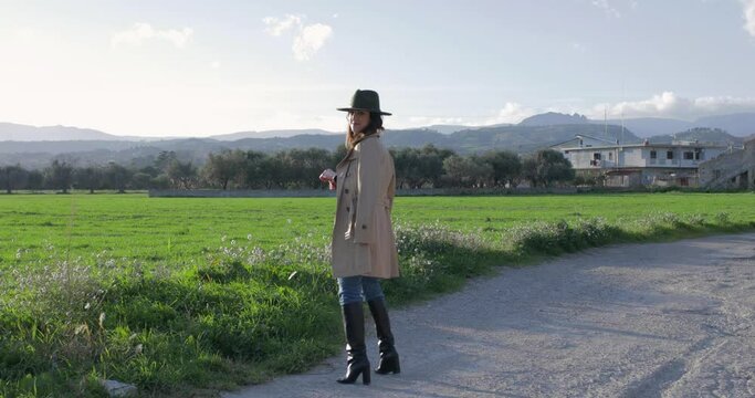 Ragazza con cappotto marrone e stivali neri in campagna
