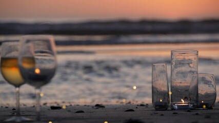 Candle flame lights in glass, romantic beach date by California ocean waves, summer sea water. Candlelight seamless looped cinemagraph. Wineglass, glass with white wine on sand. Cozy twilight lounge.
