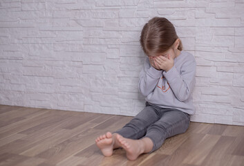 Upset little child girl crying covering face with hands sitting alone on floor, sad lonely orphan...