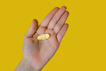 Capsules of fish oil in the palm of a person on a yellow background. A useful food supplement for improving heart function and blood clotting. Animal fat omega-3 omega-6