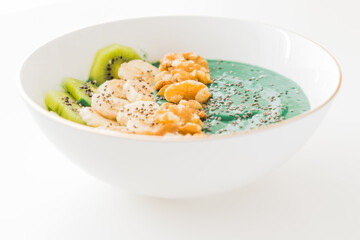 spirulina smoothie bowl with banana, walnuts, kiwi and chia seeds on white background