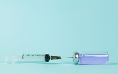 Covid-19 Recorded vaccine bottle with liquid and extracting vaccine from it with a syringe on a blue background.