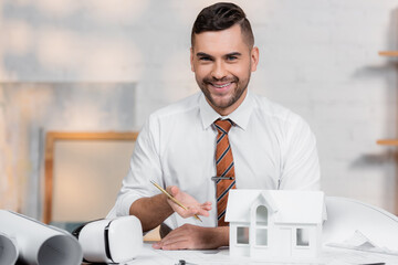 happy architect looking at camera while pointing at house model