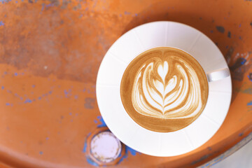 Cup of coffee with latte art pattern milk foam on metal surface