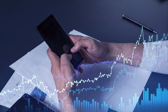 Trader holding in the hands a smart phone and researching stock market to proceed right investment solutions. Internet trading and wealth management concept. Hologram Forex chart over close up shot.
