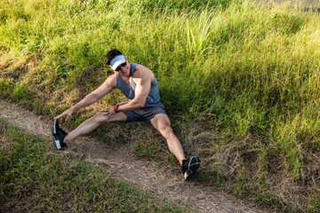 An athletic asian man does Inner thigh or adductor stretches. Stretching exercises or warmup for running outdoors.