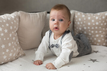 Fototapeta premium A cute little baby boy is surprised lying on the bed. Closeup portrait of newborn baby looking at camera