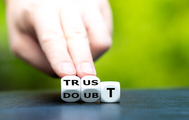 Hand turns dice and changes the word doubt to trust.