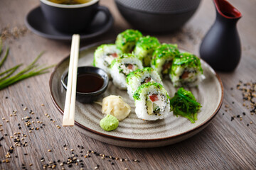 Sushi maki rolls with cucumber, avocado, tomato, creamy cheese, chuka wakame on a plate with chopsticks, soy sauce, wasabi and ginger. Japanese traditional seafood served for lunch in restaurant