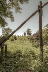 Old windmill and medieval, traditional Ukrainian rural houses on a green meadow. Blue sky with white clouds. Old photo.