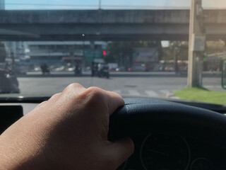 left hand is holding the steering wheel while driving car  on the street in down town to the office...
