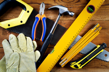 Handsaw, hammer, protective gloves, level, model knife, folding ruler  and pliers on wooden background