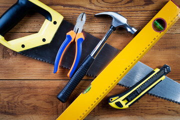 Handsaw, hammer, level, model knife  and pliers on wooden background